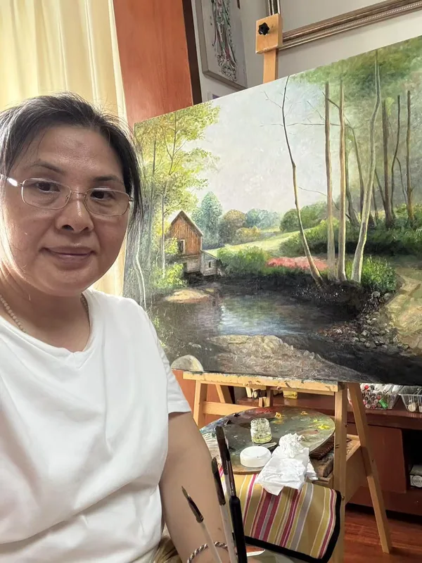 作者与画架上的绿色风景画同框